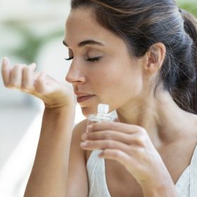 Cheerful woman girl holding a bottle of essential oil while testing it sitting on a couch at home.